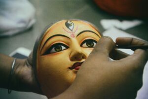 Artisan painting a traditional Durga idol mask for the Durga Puja festival.